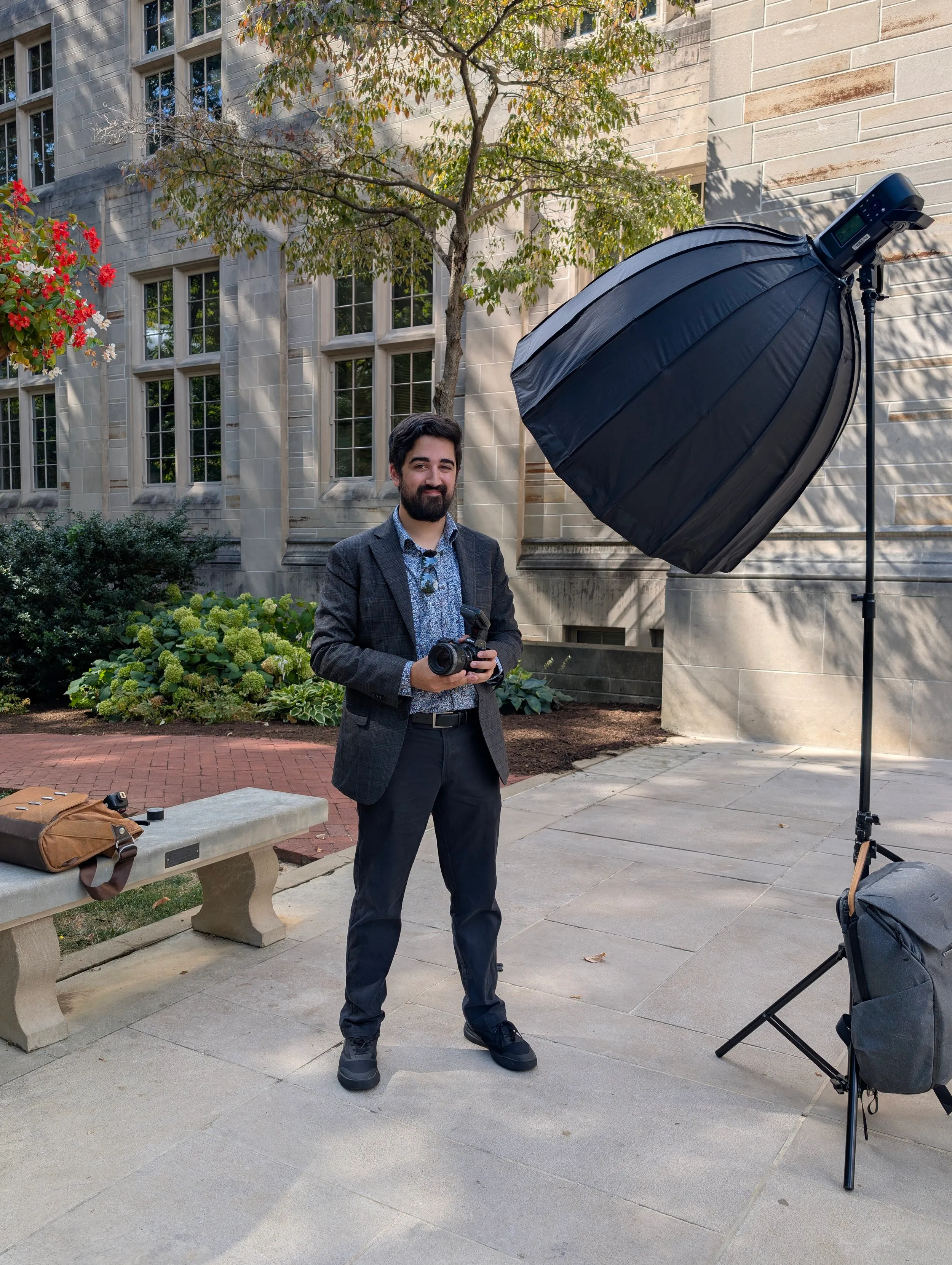Alex Kumar on location with a camera, softbox, and lighting gear outside a limestone building